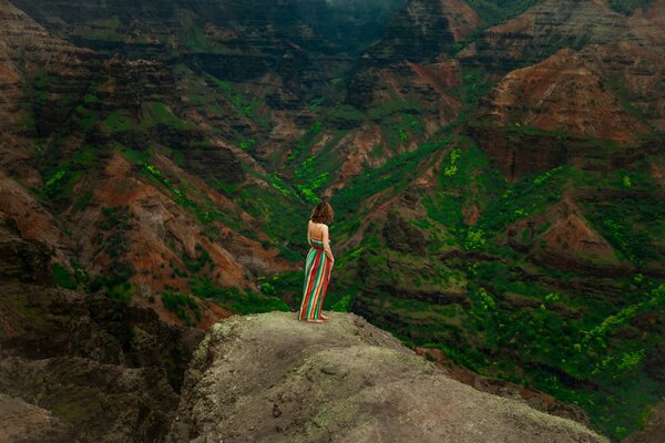Ein Mädchen in einem bunten Rock schaut auf eine Berglandschaft