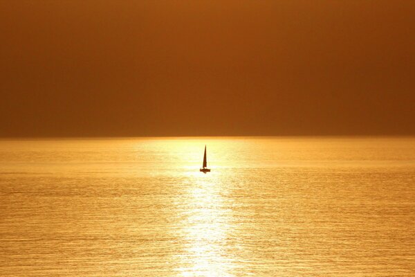 A lonely sailboat at sea at sunset