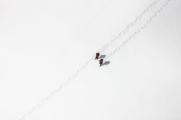 Ein Bild aus der Höhe, ein weißes Feld im Schnee, zwei Menschen gehen den Weg entlang