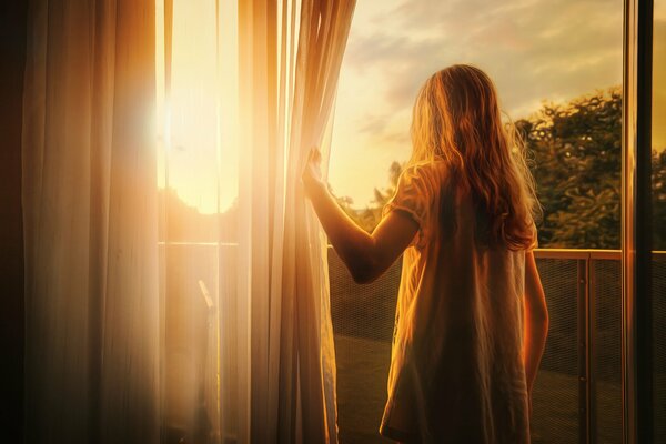 Jeune fille regardant le coucher de soleil à travers la fenêtre