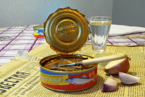 Sprat in tomato sauce, onion, newspaper, faceted glass