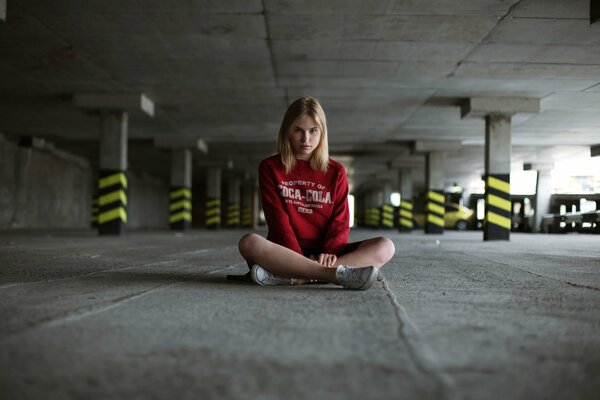 The girl is sitting on the asphalt in the parking lot