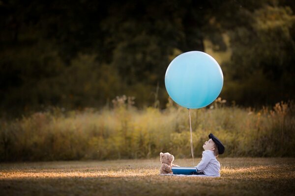 Мальчик с плюшевым медвежонком смотрит на воздушный шарик