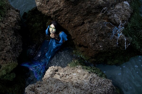 Blue mermaid in the rocks, sitting in the water