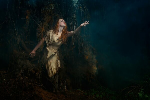 The girl at the roots of the tree looks at the misty forest