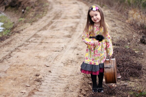 La petite fille dans une belle robe et avec une valise