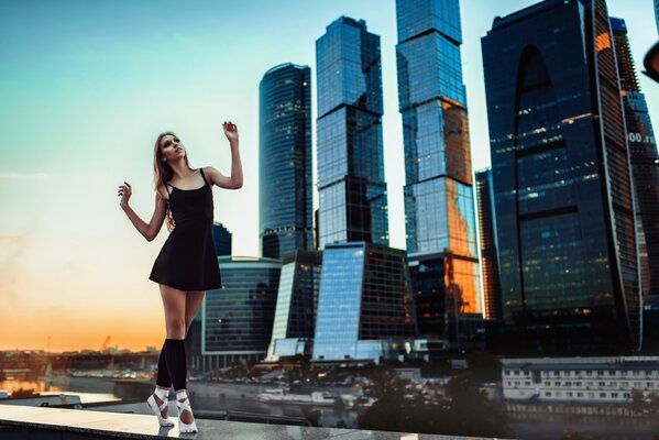 Una chica con un vestido negro y zapatos de ballet blancos de pie en el fondo de la ciudad de Moscú