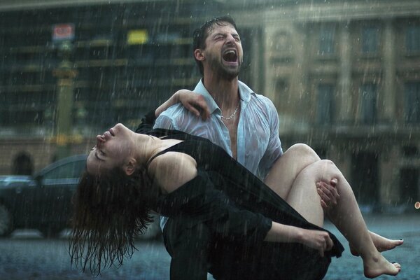 A man screams with a girl in his arms in the rain