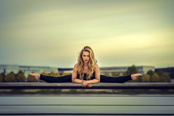 The blonde is sitting on the splits against the sky