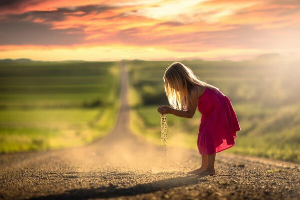 Une petite fille joue avec le sable sur la route
