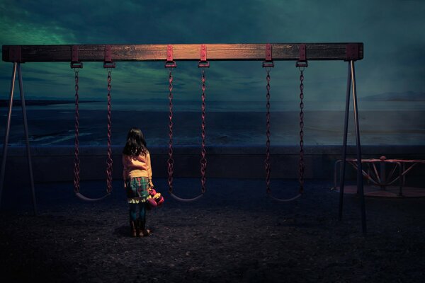A girl near a swing on the background of the sea and the night sky