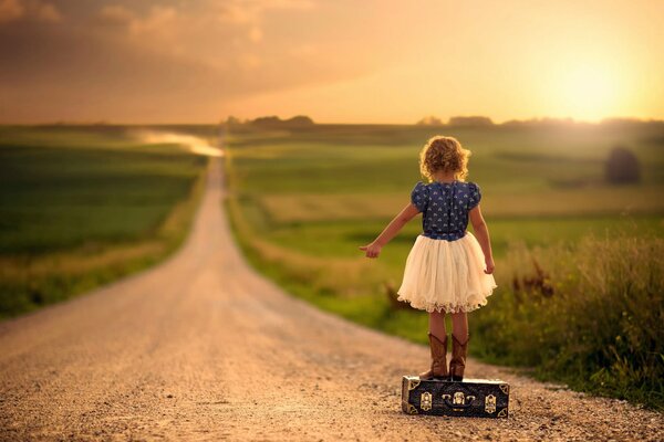 Fille debout sur une valise sur la route