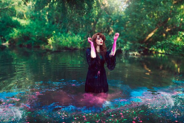 Fotoshooting für ein Mädchen in einem dunklen Kleid und mit Farbe an den Händen im Wasser