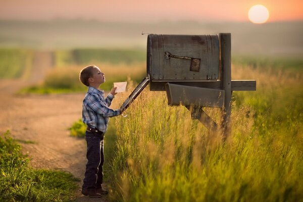 Le garçon regarde dans une grande et vieille boîte aux lettres