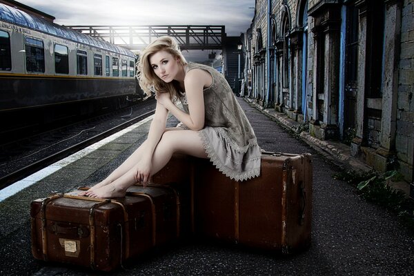 The girl is sitting on suitcases and waiting for the train