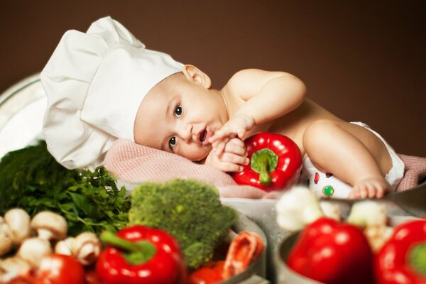 A baby in a chef s hat among vegetables