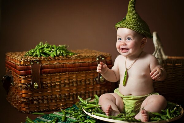 Bebé alegre sentado en un plato de guisantes
