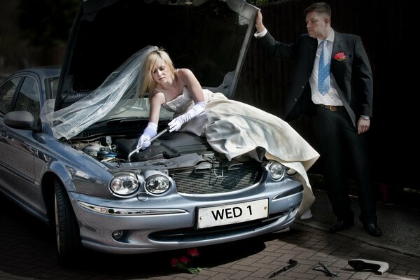 La jeune fille dans une robe de mariée répare la voiture