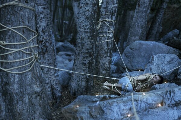 El tipo yace atado a los árboles en las rocas en el bosque