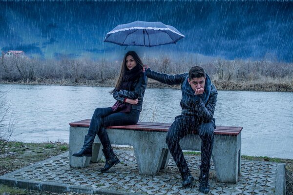 Le gars tient la jeune fille parapluie et lui-même sous la pluie