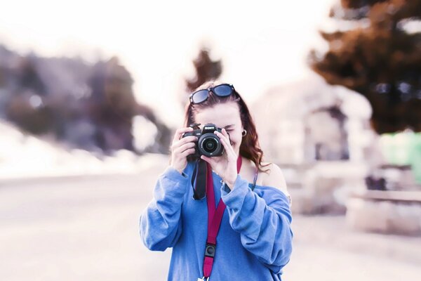 A girl in a blue sweatshirt with glasses on her head looks into the camera lens