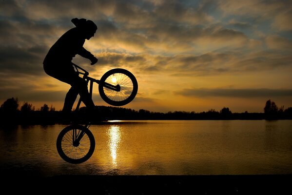 Uomo su una bicicletta al tramonto in un salto in riva al lago