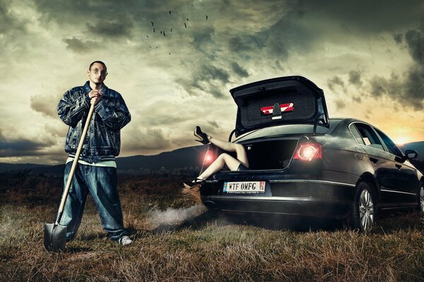 On the field there is a car with an open trunk from which women s legs stick out next to a guy with a shovel