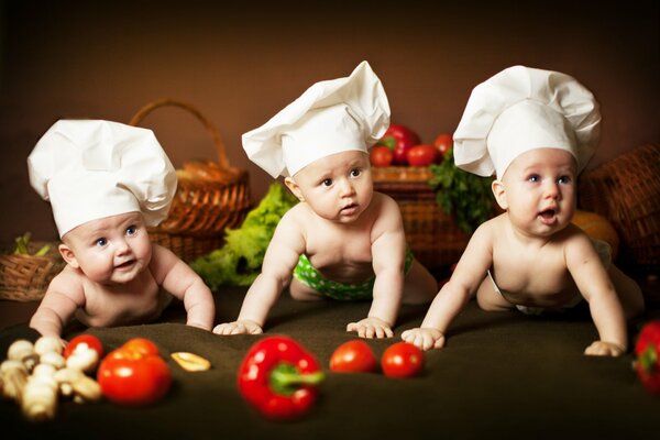 Маленькие малыши в поварских колпаках среди овощей и корзин