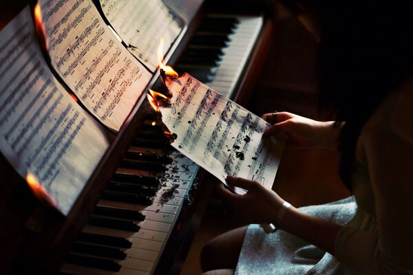 The girl is sitting at the piano and burning a sheet of music