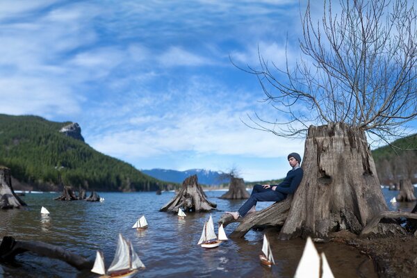 The guy is sitting leaning on a tree and looking at the boats