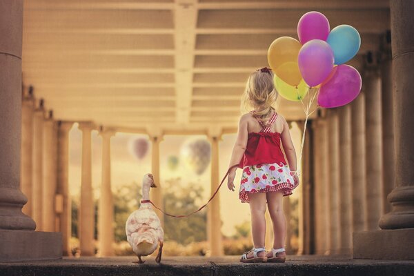 Una bambina in un vestito con bacche tiene un oca e palline colorate al guinzaglio rosso