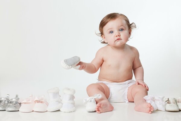 Piccolo bambino seduto sul pavimento in un pannolino vicino piccole scarpe paia di scarpe