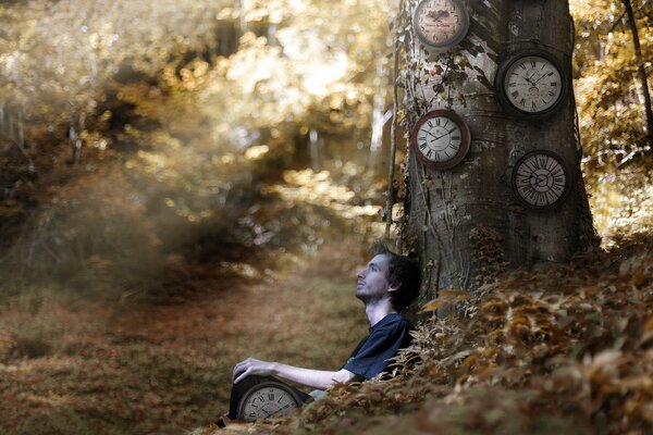 In the forest, a guy with a watch is sitting by a tree