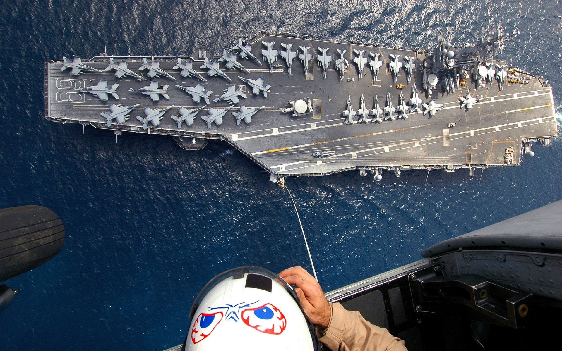 le porte-avions des avions des f-18 des bombardiers des hélicoptères l homme le câble les gens l océan la cabine châssis le casque la figure