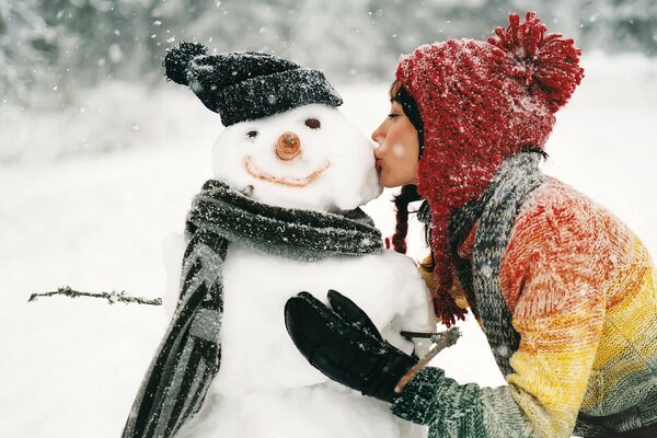 A girl kisses a snowman that she made out of snow in winter