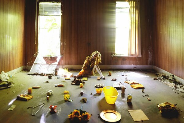 A girl with yellow wavy hair and a bow in a room with a mess and open windows