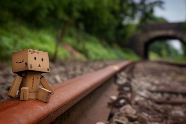 Uomo di cartone Danbo seduto sui binari della ferrovia in lontananza