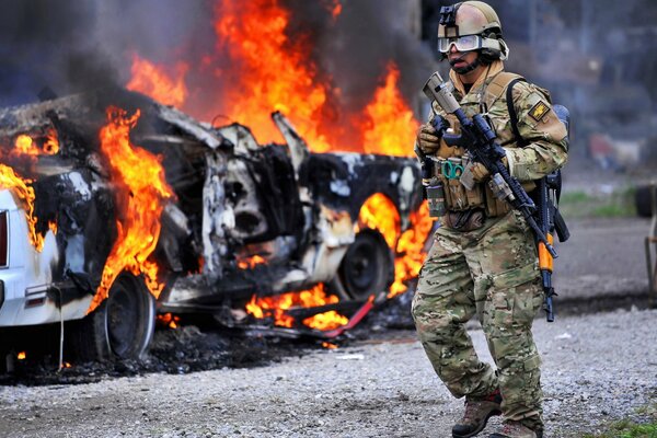 Żołnierz w pełnej amunicji N tle płonącego samochodu