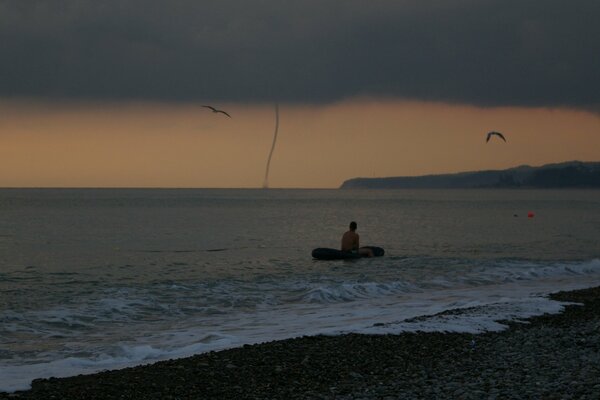 A man in a boat at sea looks at a tornado