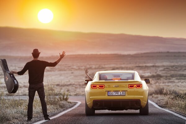 A guy with a guitar on the road near a car that left