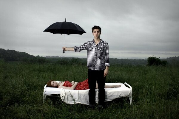 Ein Mann hält einen Regenschirm über ein liegendes Mädchen