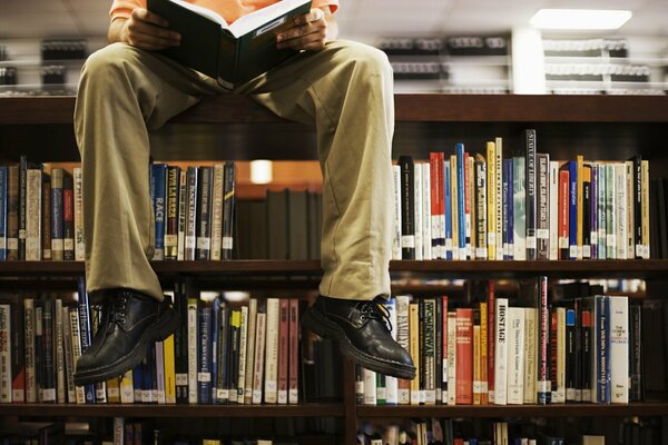 Un uomo si siede su uno scaffale in biblioteca e legge