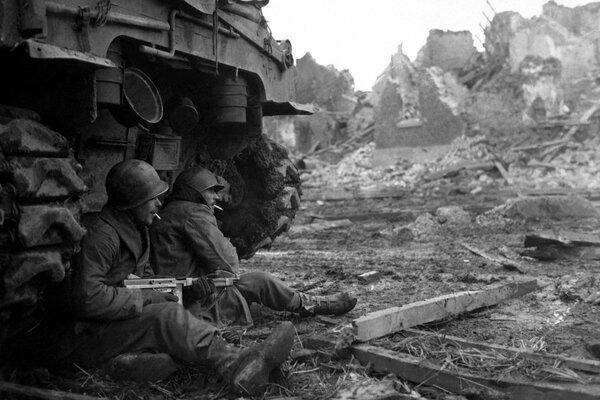 Soldiers are sitting near a tank with weapons in their hands