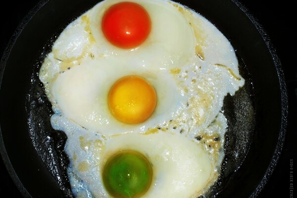 Multicolored fried eggs in a frying pan. Bright traffic light made of scrambled eggs