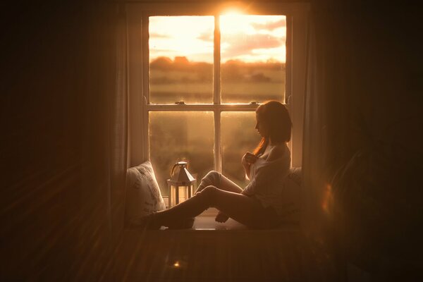 Ragazza sul davanzale della finestra sullo sfondo del tramonto