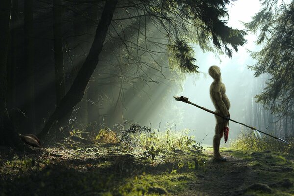 A warrior with a spear in a green forest in the rays of the sun