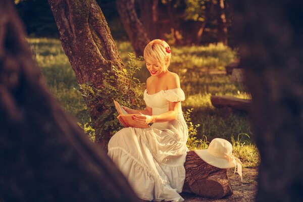 Hübsche Blondine im weißen Kleid liest ein Buch in der Natur