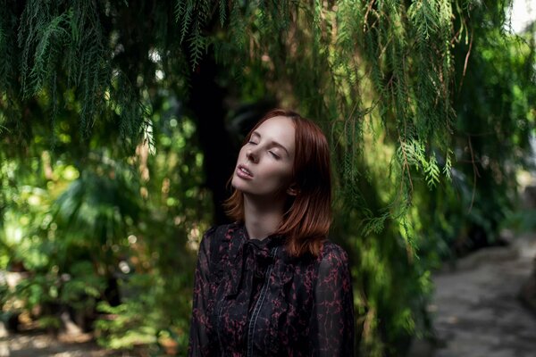 A girl with her eyes closed is standing under a tree