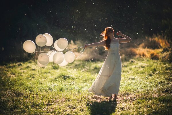 A girl in the middle of a field with balloons in her hands