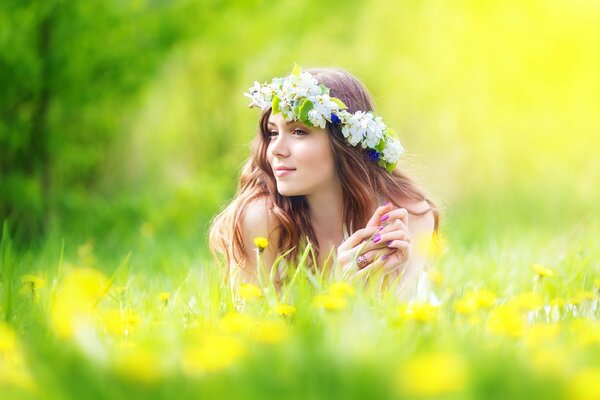 Nachdenkliches braunhaariges Mädchen in einem Kranz aus Blumen im Gras